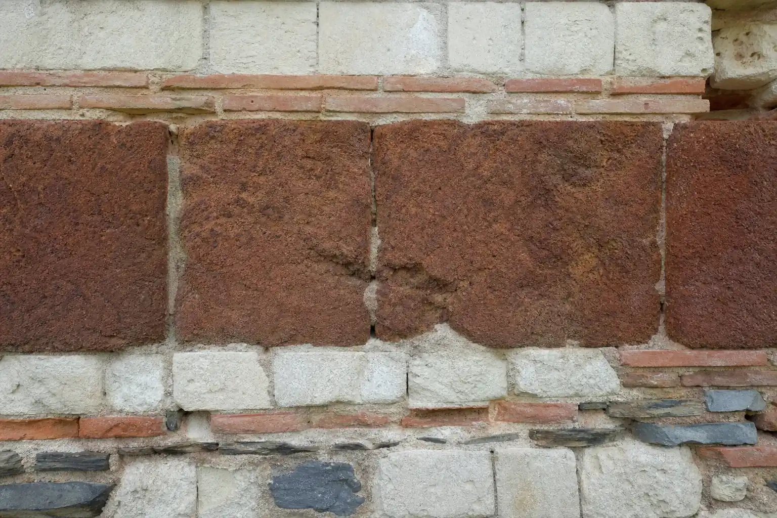 Détail d’un mur ancien : blocs de grès roussard brun roux alternés avec des assises de brique romaine rose et de calcaire clair