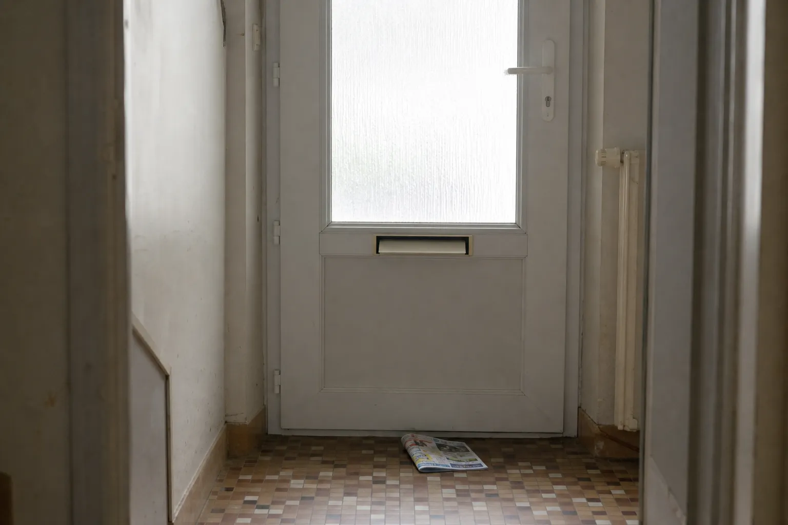 Porte d’entrée fermée vue depuis le couloir, un prospectus glissé par la boîte aux lettres posé au sol