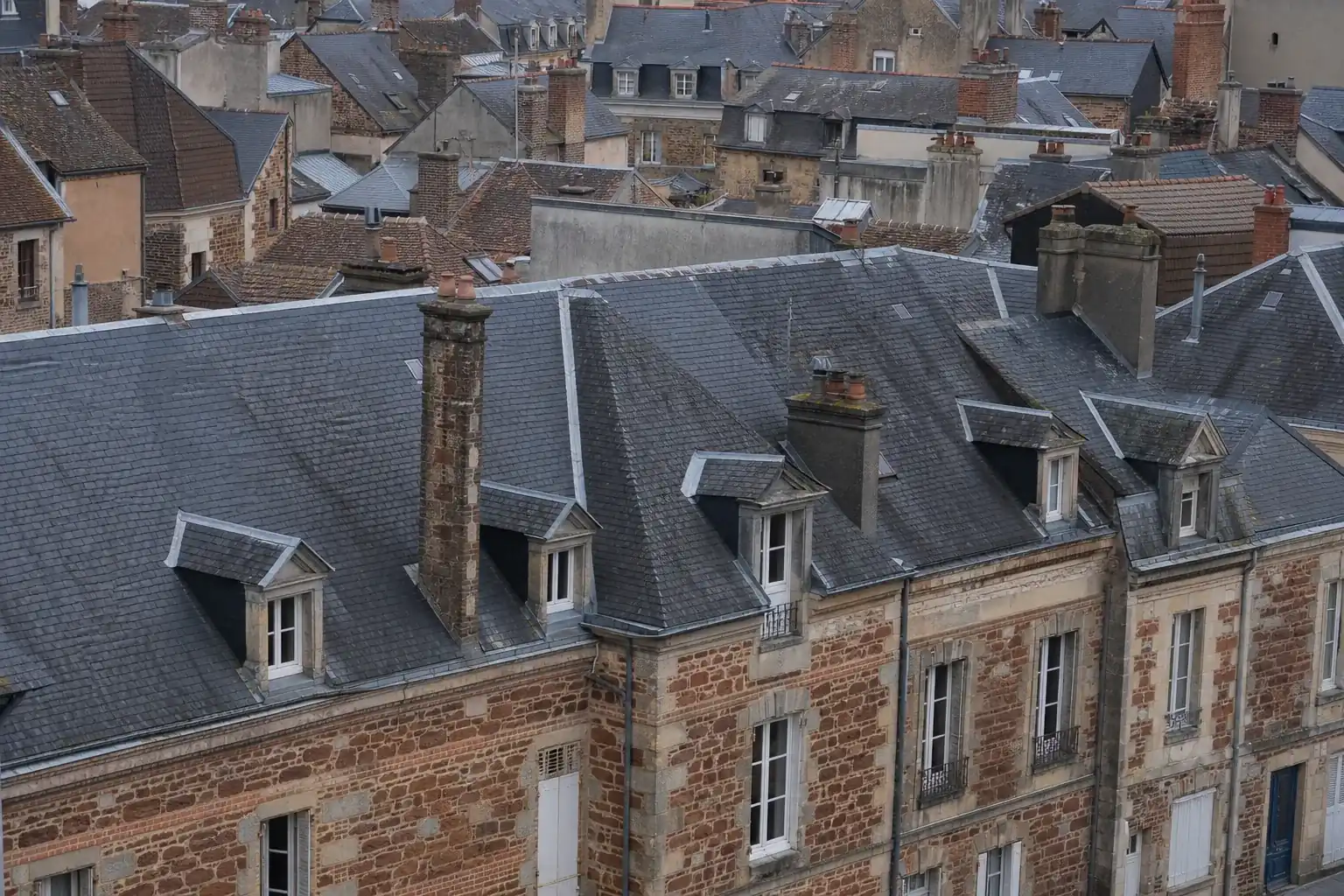 Toits d’ardoise imbriqués de la ville haute du Mans, au-dessus d’un mur de grès roussard chaîné de brique rose