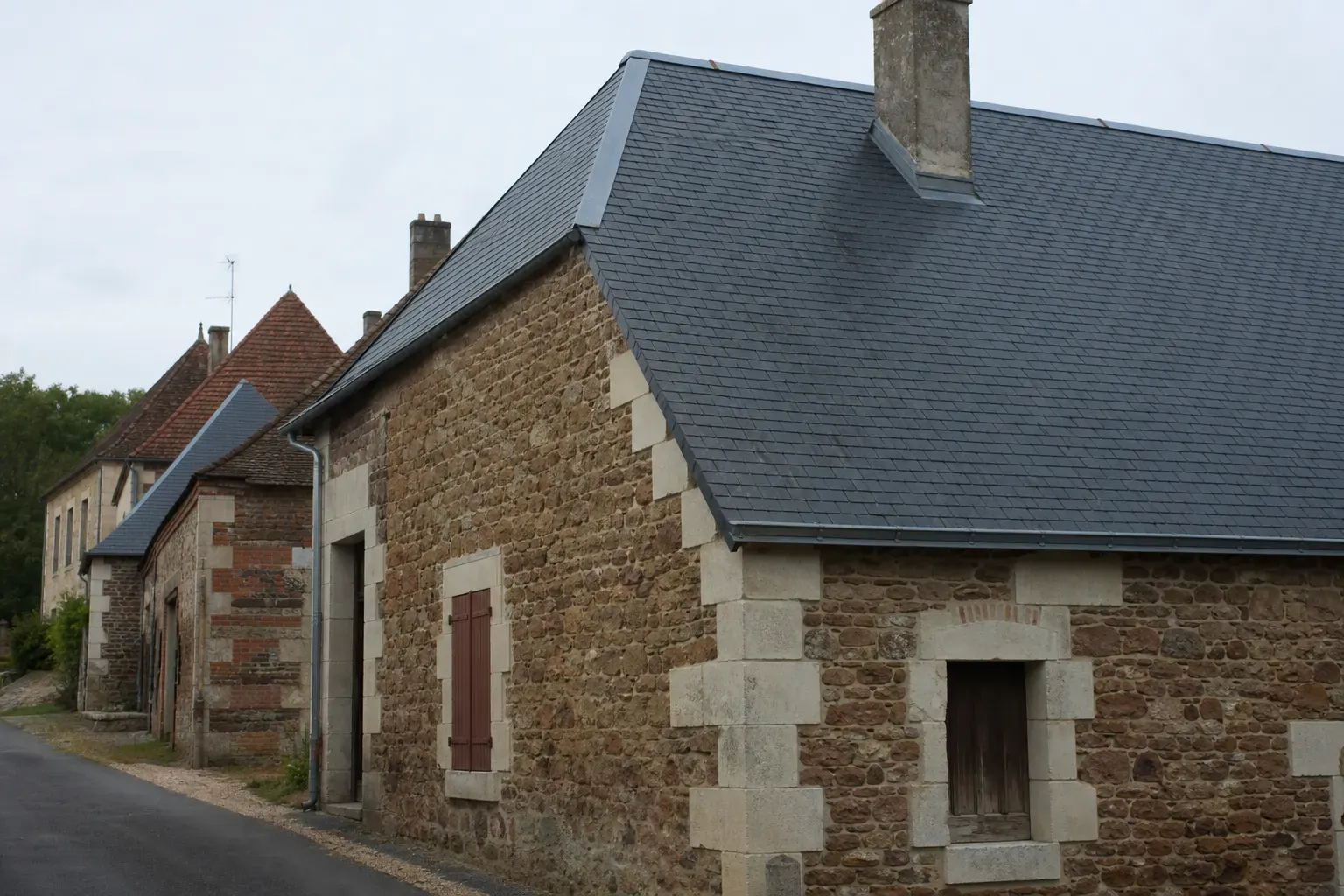 Toit d’ardoise à forte pente sur une maison de ville aux murs de grès roussard brun roux, faîtage de zinc et souche de cheminée en pierre