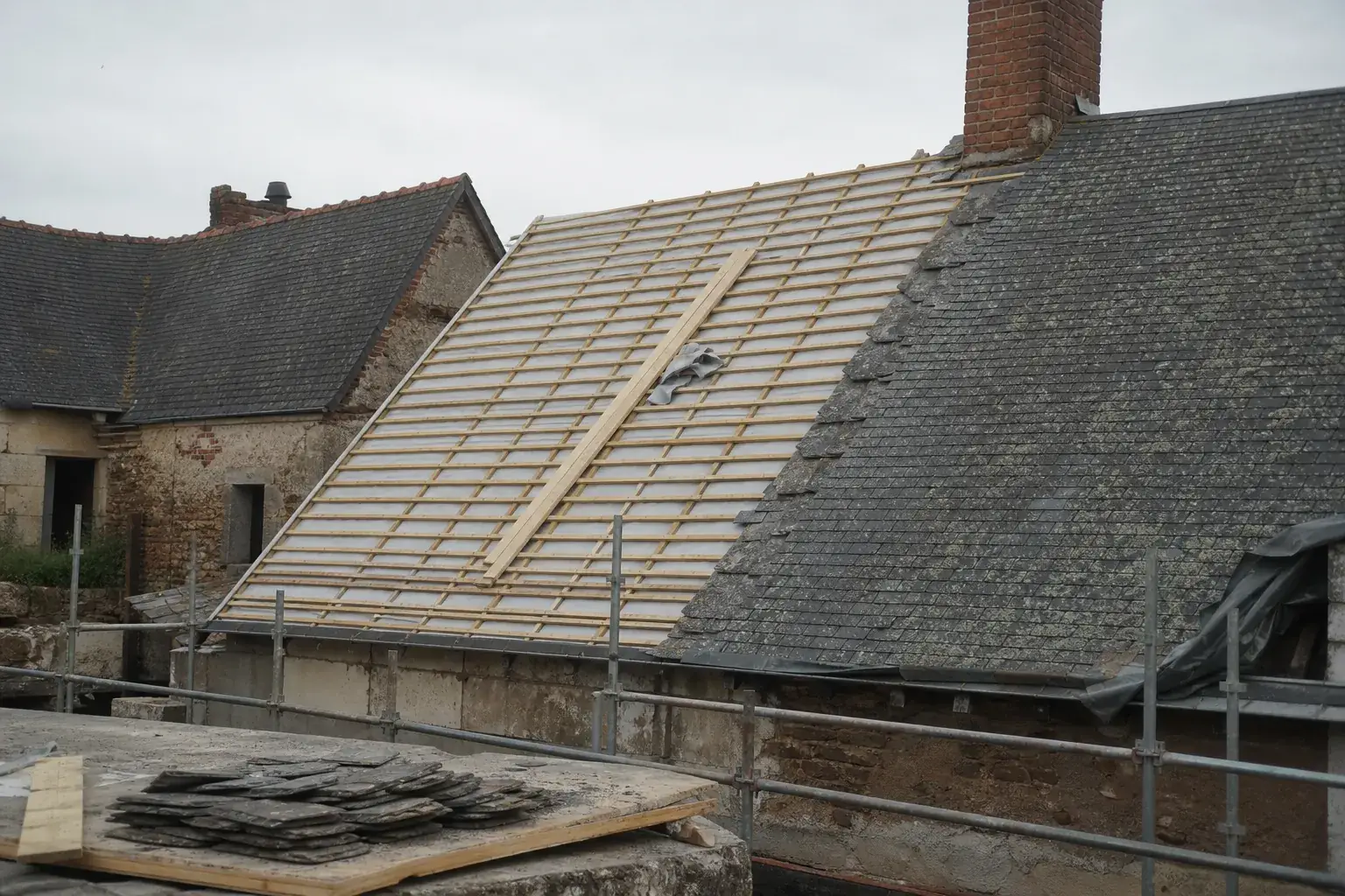 Versant à demi découvert pendant une rénovation : liteaux neufs et écran de sous-toiture d’un côté, ancienne ardoise de l’autre
