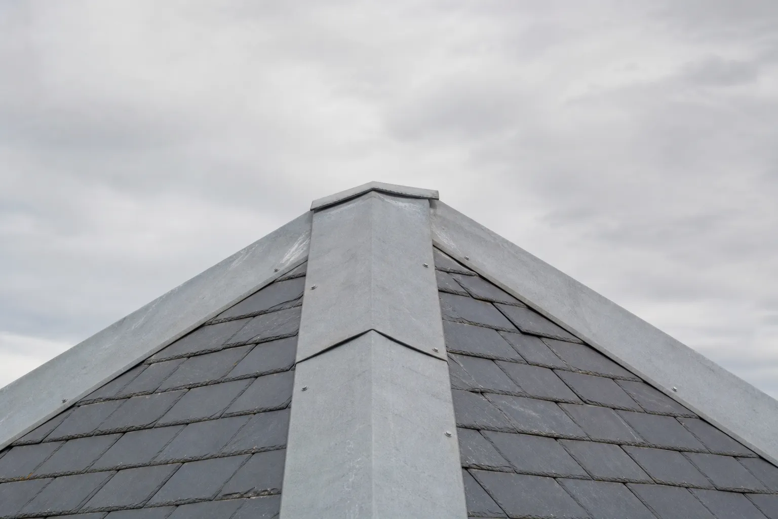 Faîtage d’ardoise coiffé d’une faîtière de zinc, dernier rang d’ardoises visible sur les deux versants