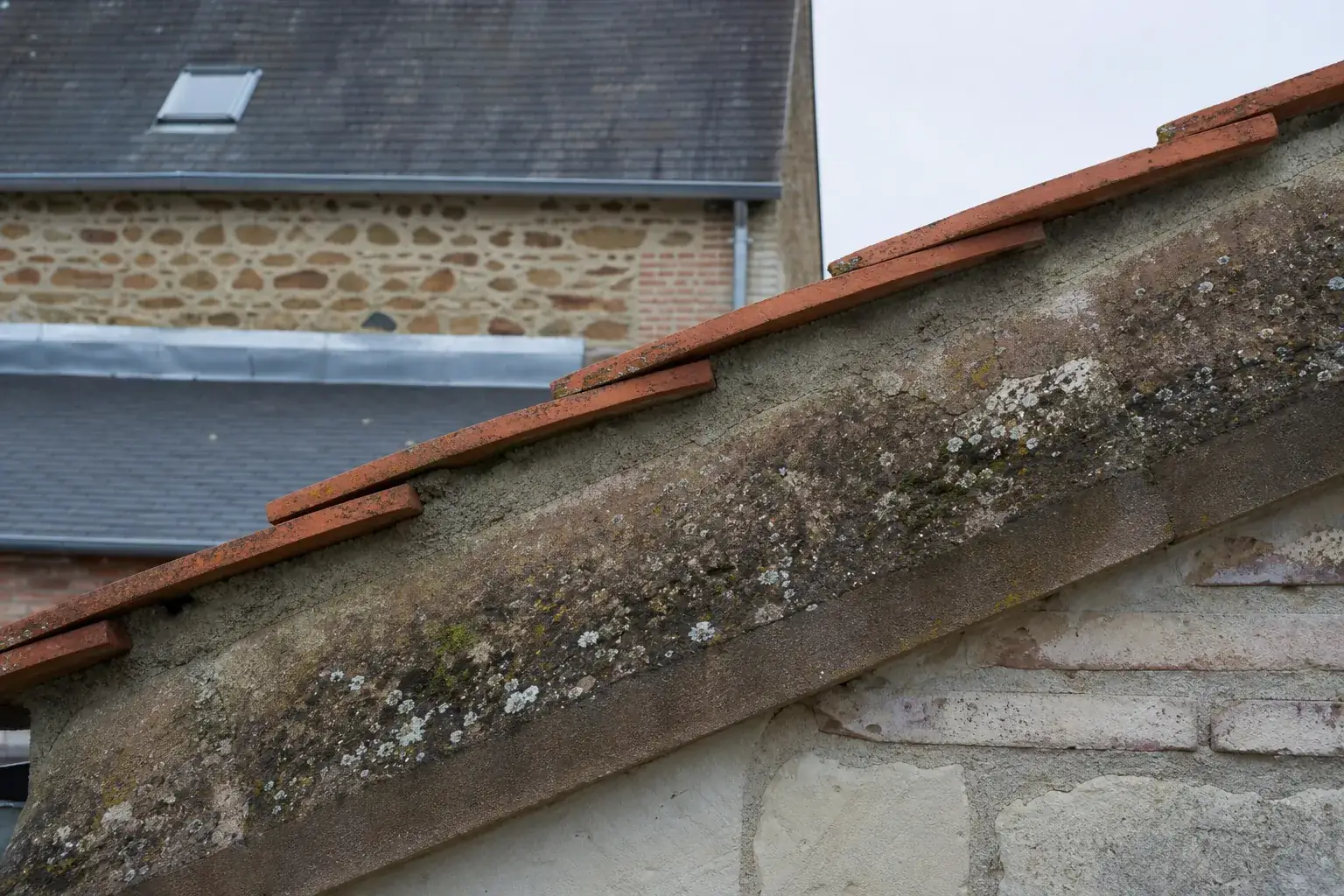 Rive de toiture au droit d’un pignon : dernier rang de tuiles plates, bain de mortier et couronnement de pierre