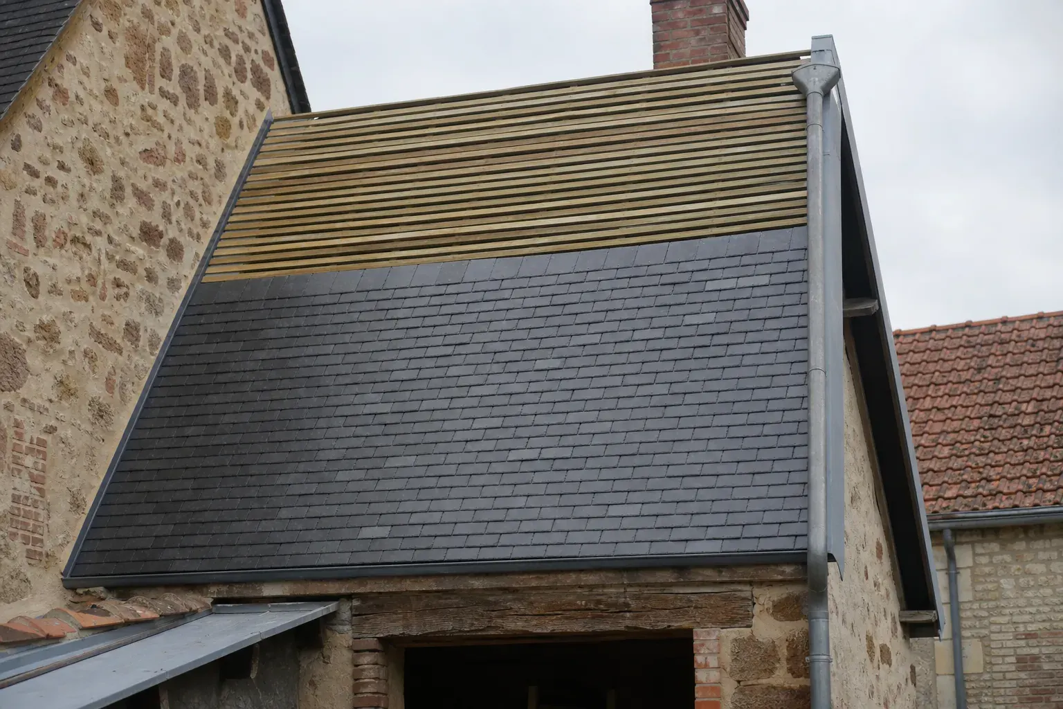 Versant d’ardoise à demi posé : deux tiers en ardoise neuve bleu gris, tiers supérieur encore en liteaux ouverts