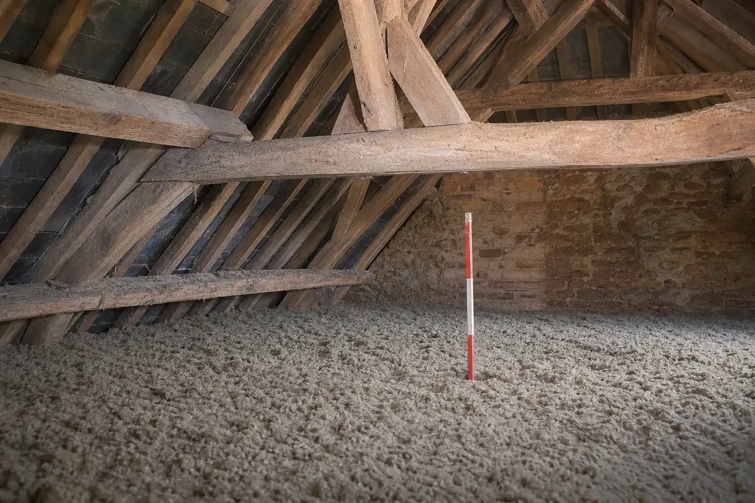 Plancher de comble couvert d’une couche régulière de laine minérale soufflée, jauge de niveau plantée dedans